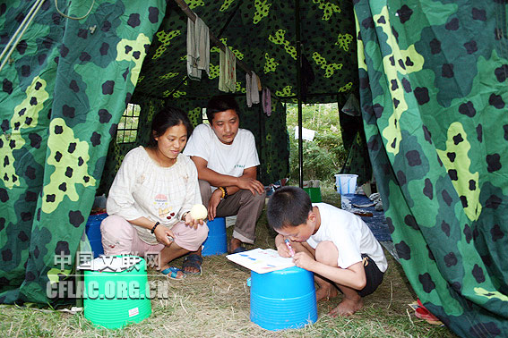九岁的成鸿钢(现就读九洲帐篷学校三一班)在防震棚门口作画。母亲罗财富和父亲成发志很喜欢儿子作画,但他们在评价孩子的作品上却意见不一。母亲认为儿子用色不太合理,父亲则认为儿子色彩用得很好。中国文联网